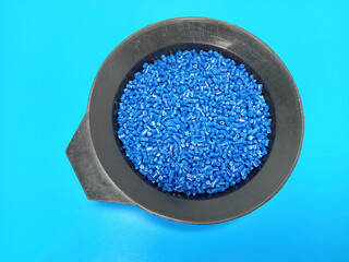 Blue masterbatch granules, polymer carrying pigment poured in a black container with a blue...