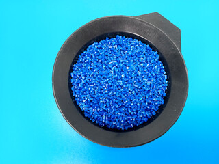 Blue masterbatch granules, polymer carrying pigment poured in a black container with a blue...