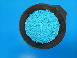 Blue masterbatch granules, polymer carrying pigment poured in a black container with a blue...