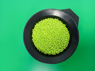 Green masterbatch granules, polymer carrying pigment poured in a black container with a green...