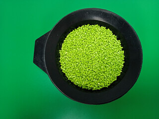 Green masterbatch granules, polymer carrying pigment poured in a black container with a green...