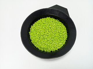 Green masterbatch granules, polymer carrying pigment poured in a black container with a white...