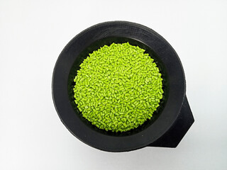 Green masterbatch granules, polymer carrying pigment poured in a black container with a white...