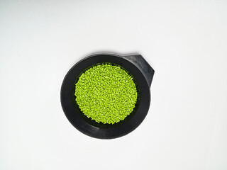 Green masterbatch granules, polymer carrying pigment poured in a black container with a white...