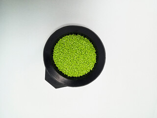 Green masterbatch granules, polymer carrying pigment poured in a black container with a white...