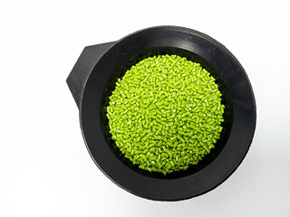 Green masterbatch granules, polymer carrying pigment poured in a black container with a white...