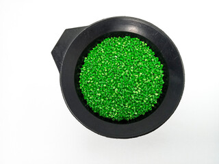 Green masterbatch granules, polymer carrying pigment poured in a black container with a white...