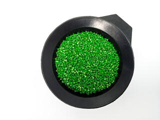 Green masterbatch granules, polymer carrying pigment poured in a black container with a white...