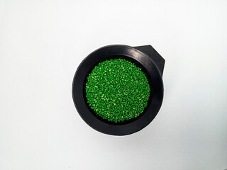 Green masterbatch granules, polymer carrying pigment poured in a black container with a white...