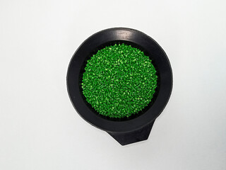 Green masterbatch granules, polymer carrying pigment poured in a black container with a white...