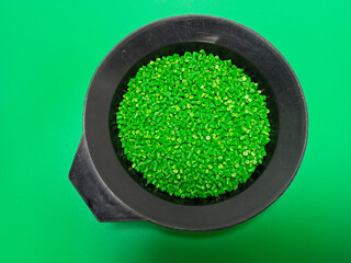 Green masterbatch granules, polymer carrying pigment poured in a black container with a green...