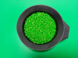 Green masterbatch granules, polymer carrying pigment poured in a black container with a green...