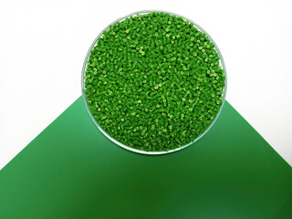 Green masterbatch granules in a glass container, the polymer carries the pigment poured in a green...