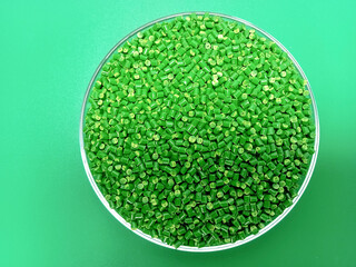 Green masterbatch granules in a glass container, the polymer carries the pigment poured in a green...