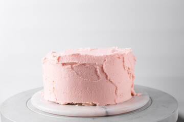 Cake being covered in pink buttercream frosting, cake being covered in pink american buttercream, process of decorating a cake