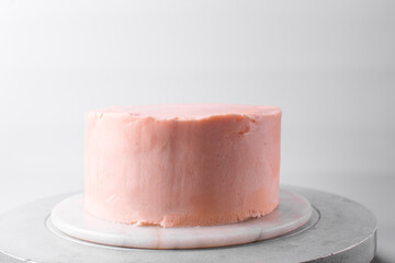 Cake being covered in pink buttercream frosting, cake being covered in pink american buttercream, process of decorating a cake