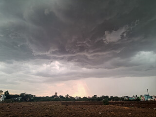 Fototapeta premium Dark Monsoon Clouds Over Rural Landscape with Faint Rainbow Glow