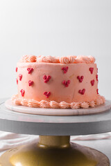 Pink buttercream cake covered in buttercream hearts on a cake stand