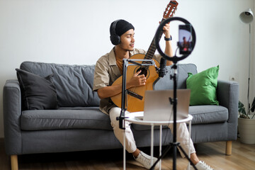 Fototapeta premium Young Asian Influencer Playing Acoustic Guitar And Singing During Live Online Broadcast
