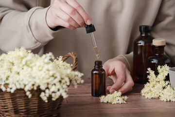 A person carefully processes elderflower in a cozy workshop, surrounded by dark glass bottles and a basket filled with the vibrant blossoms. Alternative medicine, healthy and well-being theme concept.