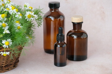 Three brown glass bottles arranged artfully alongside a basket of chamomile flowers. Natural...