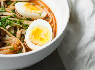 Overhead view of spicy noodle soup with eggs and beef chunks in a white bowl, top view of noodles eggs in a spicy broth with scallions