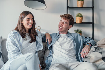 Young happy couple having fun talking laughing relaxing at home on couch, boyfriend embracing...