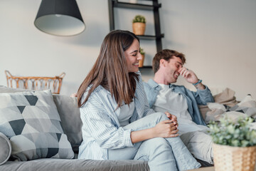 Young happy couple having fun talking laughing relaxing at home on couch, boyfriend embracing...
