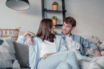 Portrait of young 20s just married couple in love posing photo shooting seated on couch in modern...