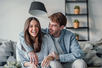 Head shot positive loving bonding married couple sitting on comfortable sofa, looking at camera, holding video call with friends. Happy family bloggers recording video for personal channel at home.