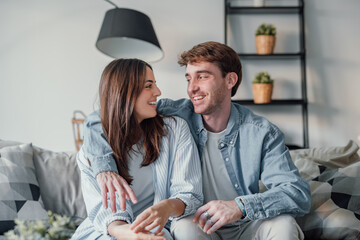 Head shot positive loving bonding married couple sitting on comfortable sofa, looking at camera, holding video call with friends. Happy family bloggers recording video for personal channel at home.
