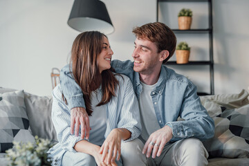 Portrait of young 20s just married couple in love posing photo shooting seated on couch in modern...