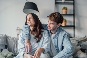 One dream for two of us. Romantic millennial spouses relax on couch together looking aside...