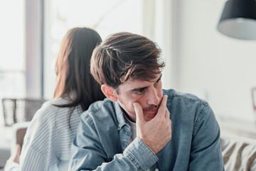 Attractive man is depressed, sitting on the couch ignoring woman, having a dispute with wife or...