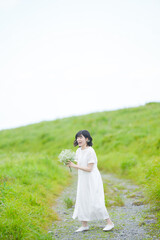 A woman in her thirties with midlength hair in a white dress stands on a mountain trail, gently...