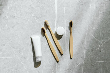 Top view of eco-friendly bamboo toothbrushes and toothpaste in white tube on grey marble...