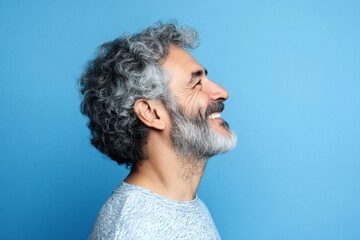 Fototapeta premium A man with a soft expression in a peaceful setting. Blue solid background. Fashionable men's two-block cut haircut - midlife arabian man with curly hair. Artwork of style for aging men.