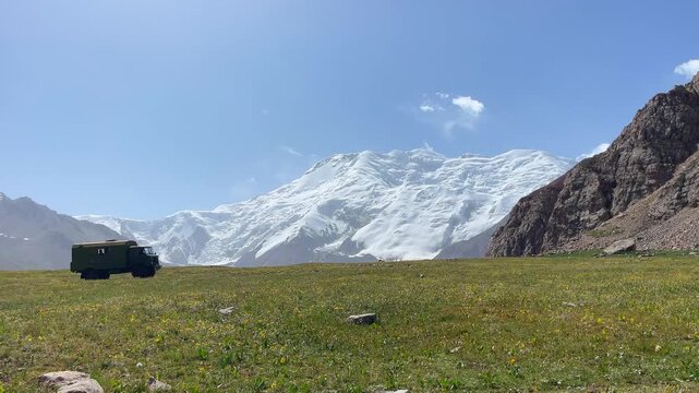 Incredible wide angle panoramic 4K video shot of Pamir mountains range near from Lenin peak base camp at cca 3800m with slowly moving milytary colors truck driving mountain road on Onion meadows field