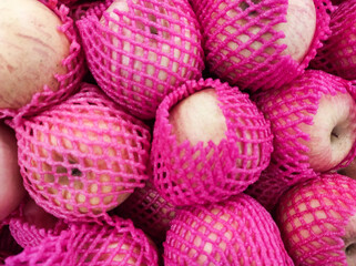Close-up shot of Fuji apples wrapped with pink PE Foam in grocery store. A pile of apples covered by a fruit net to protect them from bumps and scratches. Graphic Resources. Advertisement space