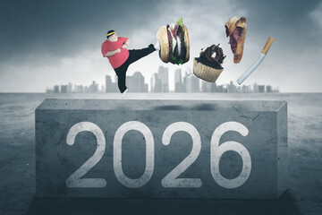 Overweight man kicking away junk food and a cigarette above a concrete block with 2026 text.