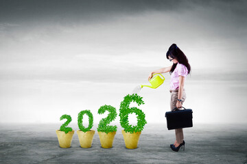Businesswoman watering potted plants shaped as the year 2026.