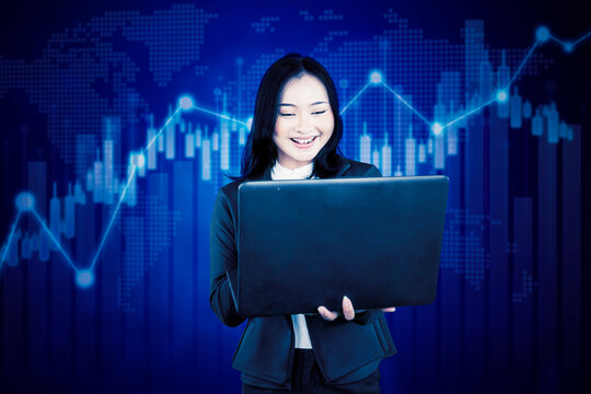 Happy businesswoman analyzing stock market data on a laptop with a global chart background