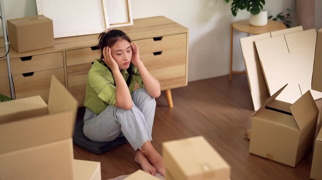 Asian adult woman feels exhausted moving relocating into new home surrounded by unpacked boxes depicts stress and challenges of life transitions