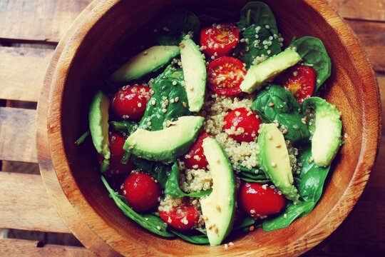 Wooden bowl brimming with quinoa, spinach, avocado, and cherry tomatoes