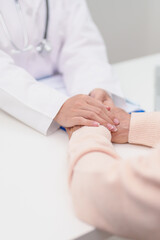 doctor holding hands with elderly female patient, showing empathy and support during a medical...