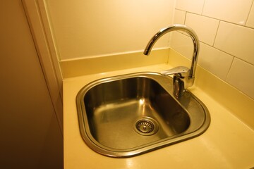 Clean stainless steel sink with curved chrome faucet set in a beige countertop under warm lighting...
