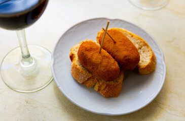 Simple and hearty snack is served on plate - two thick slices of bread and cutlets. Bamboo toothpicks are inserted into cutlets for convenience. Dish is complemented by glass of cold beer.