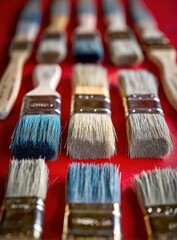 A Painter's Arsenal: Worn Brushes in Formation on a Vibrant Red Canvas.