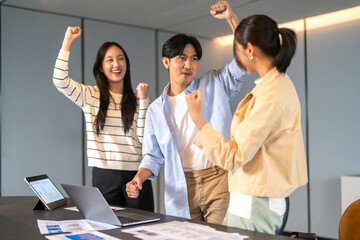 Asian business team celebrating success with raising fist in office, joyful expression teamwork...