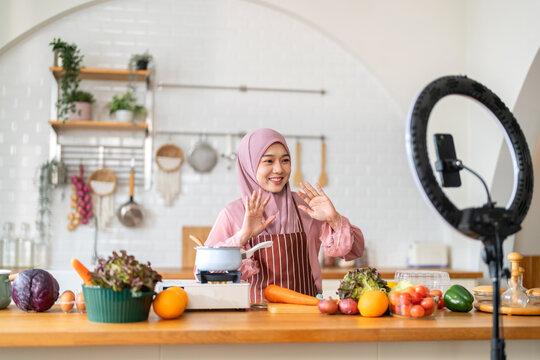 Muslim woman vlogger live streaming cooking online in kitchen look at camera with vegetables, content creator culinary class at home studio, halal food influencer cooking live, video for social media